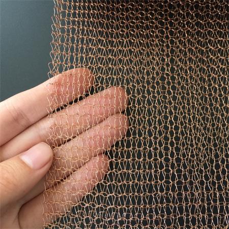 A hand is holding the knitted copper mesh with even structure on the black ground.