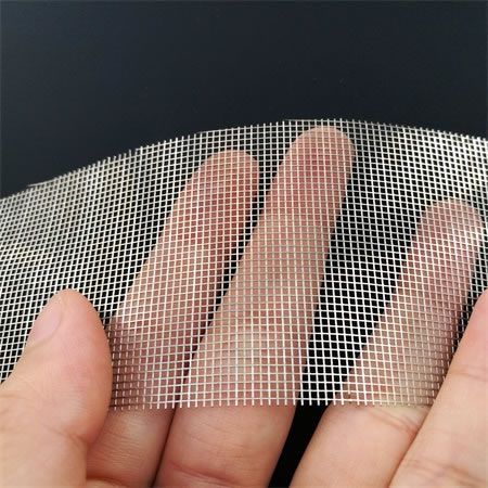 A piece of Nickel 200 wire mesh held by a hand on the black ground.